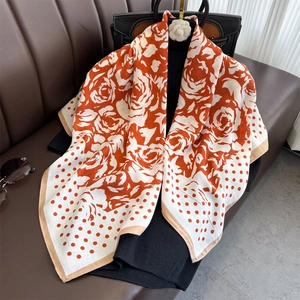 Polka dot camellia silk scarf in orange and white floral print draped on a leather bag