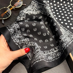 Close-up of black silk scarf featuring white paisley patterns and smooth satin texture