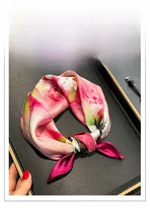 Détail d'un carré de soie noué en boucle avec des motifs floraux roses et verts
