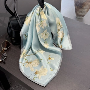 Elegant silk scarf with white magnolia print on light blue, styled on a luxury leather bag