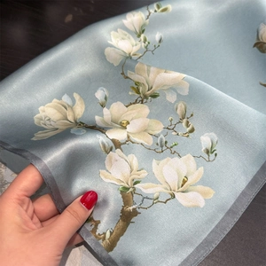 Detailed macro view of light blue silk scarf featuring realistic white magnolia flower prints