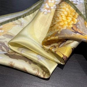 Detailed view of yellow silk scarf with chrysanthemum floral patterns and green edges