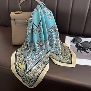 Detail of a blue floral silk scarf elegantly tied to a handbag handle as a stylish accessory