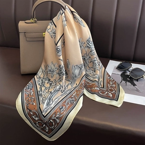 Elegant champagne silk scarf with black floral tulip patterns draped over a leather handbag
