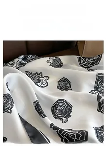 Close-up of elegant white satin scarf featuring large black rose print on leather surface