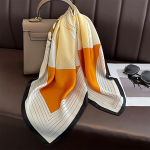 Elegant geometric silk scarf with yellow and orange blocks tied to a stylish handbag