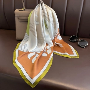 Elegant silk scarf with orange and lime geometric patterns draped on a handbag