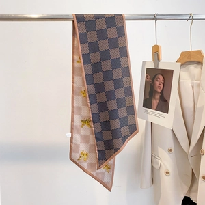 Détail d'un foulard étroit en soie avec monogramme bleu et motifs d'abeilles roses