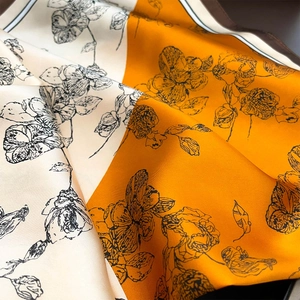 Detailed view of orange and beige silk scarf with hand-drawn floral prints and high sheen