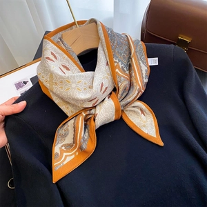 Elegant paisley print silk scarf in orange and grey draped on a stylish wooden hanger