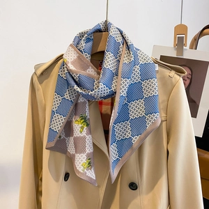 Petit foulard en soie imprimé bleu et marron porté sur un trench-coat classique beige