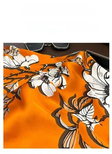 Macro shot of silk scarf fabric featuring orange floral patterns and satin luster detail