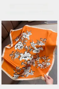 Detail of elegant orange silk square scarf with white floral print on leather background