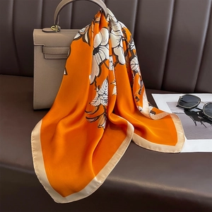 Elegant orange silk scarf with white floral patterns draped on a grey handbag