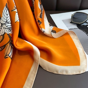 Detailed shot of orange silk scarf with leaf pattern texture next to sunglasses