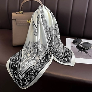 Elegant white silk scarf with floral pattern draped on handbag with sunglasses