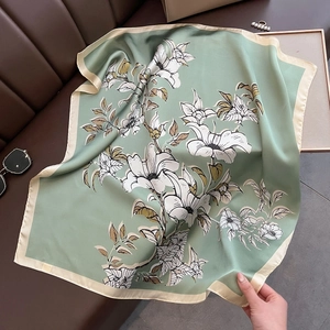 Close-up of sage green silk scarf with white floral patterns on a dark leather surface