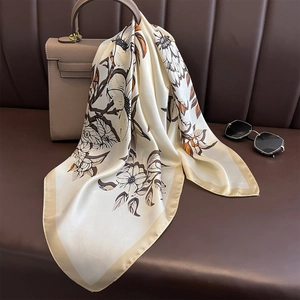 Elegant floral silk scarf in cream and orange draped on a leather bag for styling