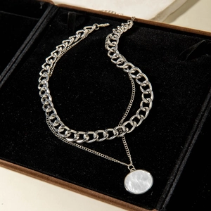 Detail of layered silver Cuban chain with round white mother of pearl pendant on velvet