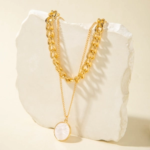 Gold double-layered necklace with round white shell pendant on stone display