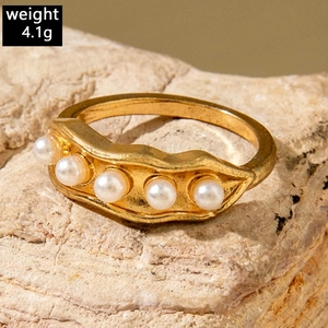 Macro detail of a golden pea pod ring with white pearls on a natural stone background