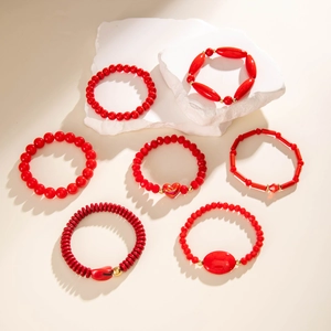 Detail of seven red beaded bracelets with gold spacers and heart pendant on stone stand