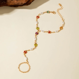 Detailed shot of gold finger-to-wrist bracelet with colorful enamel butterflies and pearls