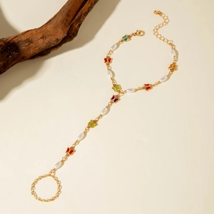 Detail view of gold hand chain featuring colorful butterflies and white pearls on wood