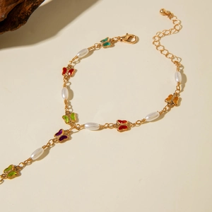 Close-up of golden hand chain featuring colorful butterflies and white faux pearls