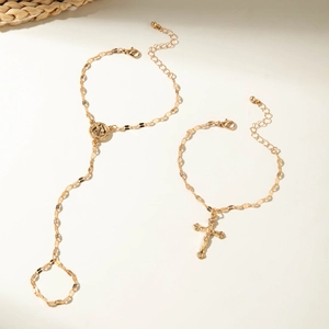 Detail of gold-plated cross bracelet and finger ring chain set on beige background
