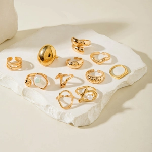 Detailed set of 11 golden alloy rings with pearls on white stone slab background