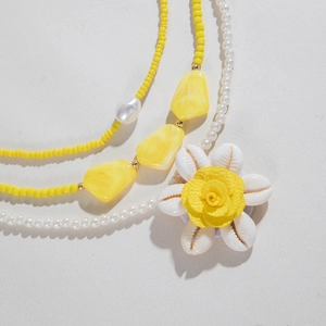 Gros plan sur des colliers bohèmes en perles avec fleur en coquillage et pendentif jaune