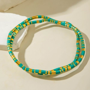 Detail of bohemian teal clay bead necklace with golden spacers on a beige stone