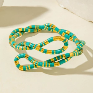 Macro shot of turquoise and gold heishi beads on a textured stone surface with deep shadows