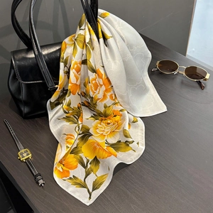 Floral luxury silk scarf with yellow flowers elegantly draped over a black leather handbag
