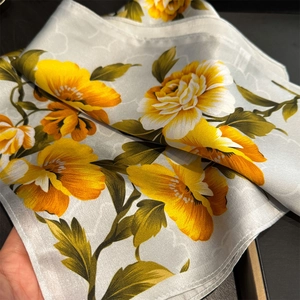 Detail of silk scarf showing orange flower print and smooth satin texture on gray fabric