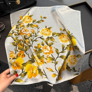 Luxurious silver grey silk square scarf with yellow floral pattern on a dark desk