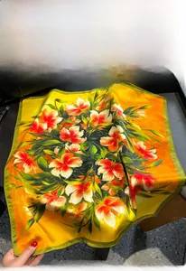 Close-up of silk square scarf featuring vibrant orange lily prints and smooth satin texture
