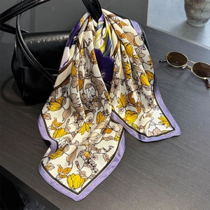 Silk floral scarf with purple trim draped over a black leather luxury handbag