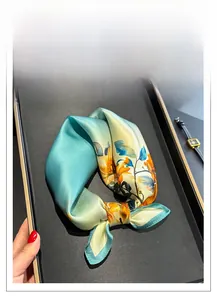Macro detail of floral silk scarf featuring bright orange flowers and mint green silk fabric