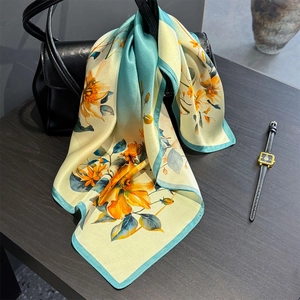 Silk square scarf with floral print draped over a black leather handbag with accessories