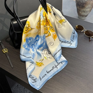 Floral silk square scarf with blue waves and yellow roses tied on a black leather handbag