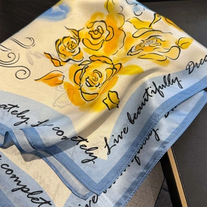 Elegant silk scarf with yellow rose pattern and artistic lettering on black table
