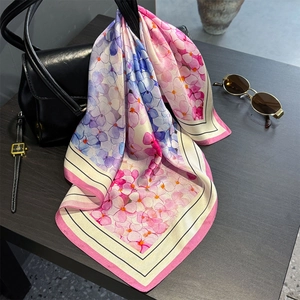 Silk square scarf with hydrangea floral print draped on a black leather handbag