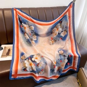 Floral square silk scarf with orange and blue contrast borders on a brown leather sofa