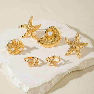 Detail shot of 6-piece golden sea shell ring set with pearls on a stone display