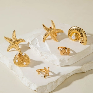 Golden starfish and seashell ring set with pearls on white stone display platforms