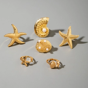 Detailed close-up of golden sea star and shell rings with pearls on a grey background