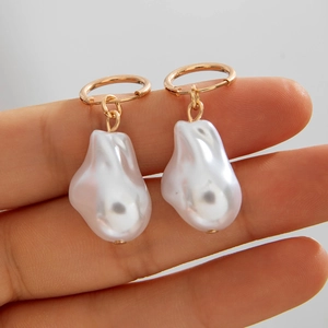 Detail showing natural baroque pearls and elegant gold hooks held by fingers