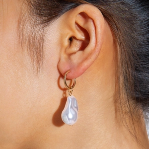 Close-up of golden hoop earrings with high-luster white baroque pearls on a model